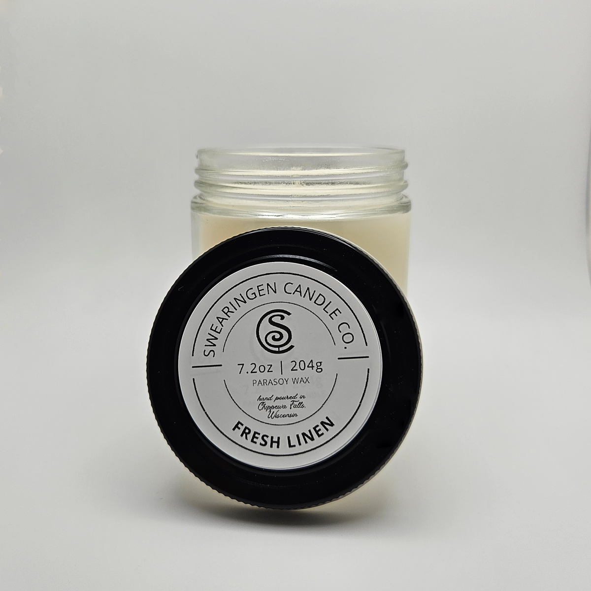 Fresh Linen hand-poured parasoy candle in a clear glass jar with a black lid, shown in a three quarter view - Swearingen Candle Co.
